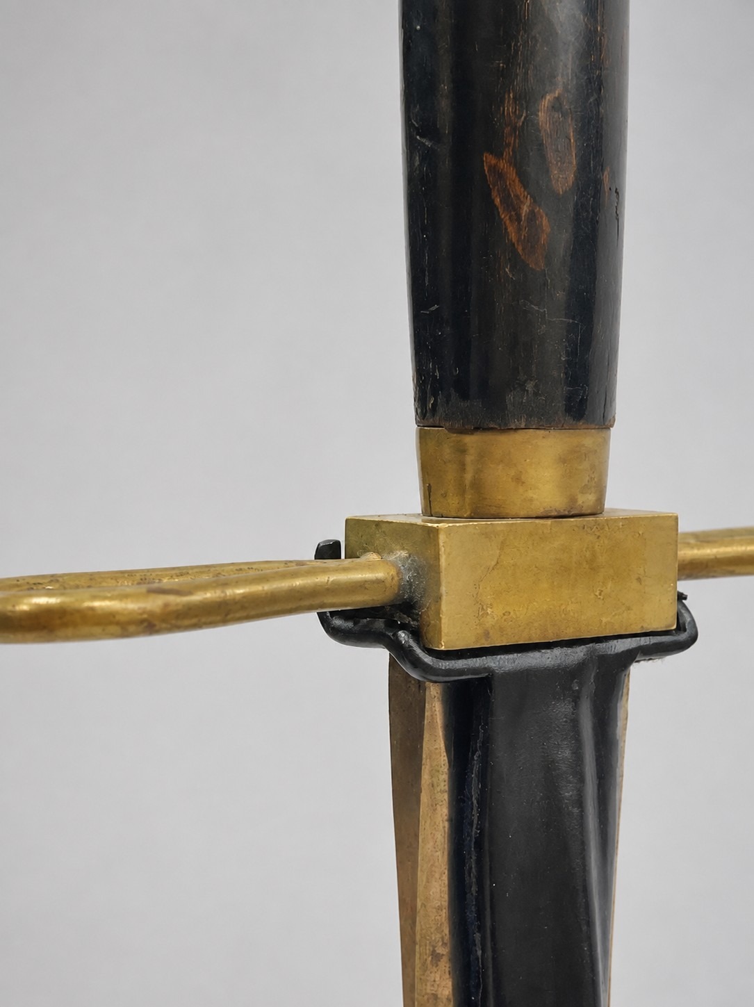 Close-up of the sword's black-painted wooden grip and brass ferrule seated in the mount's rear bracket.