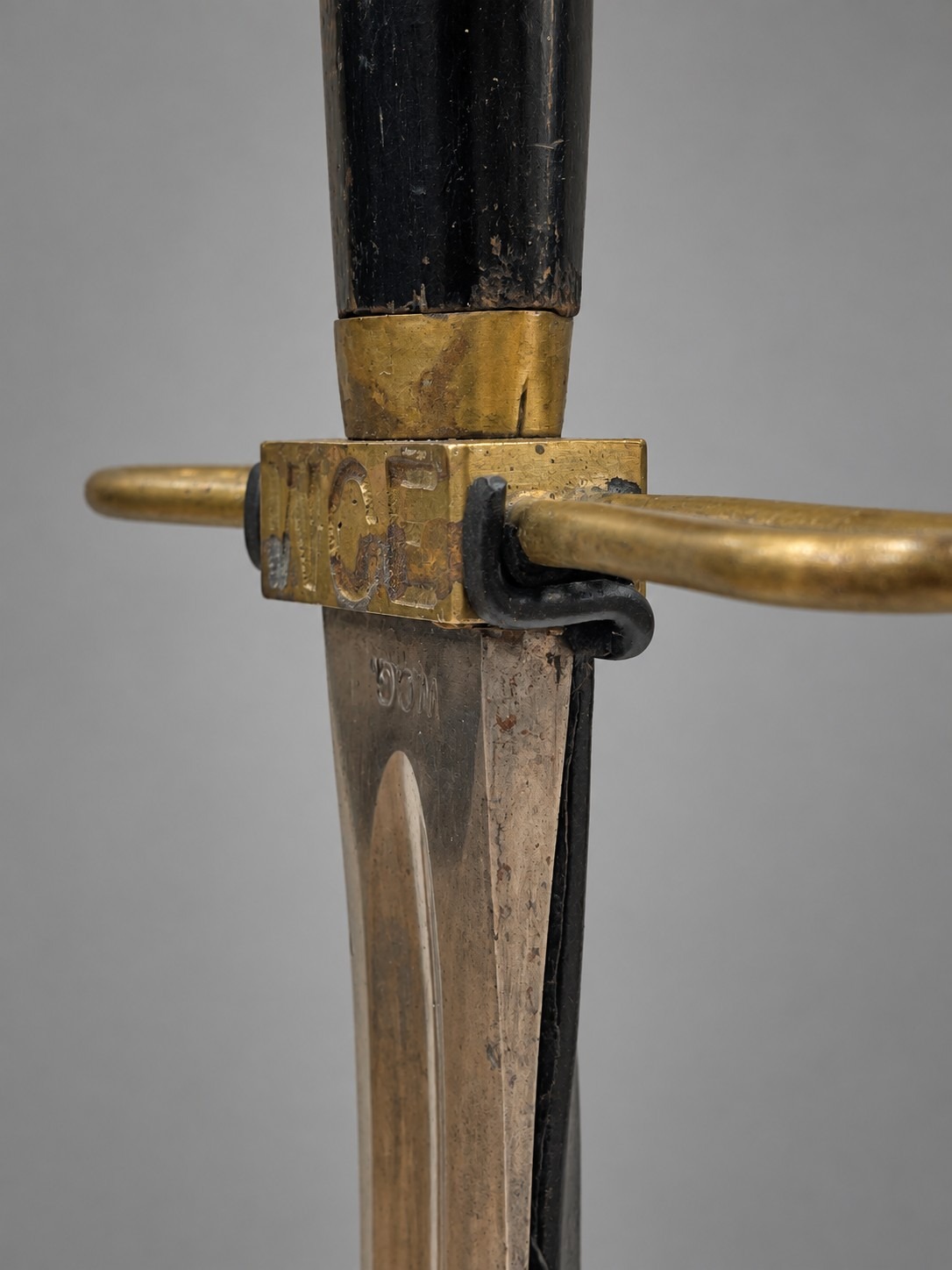 Close-up of the sword's brass hilt and cross-guard resting in the custom mount's fitted bracket, showing the "WCE" stamp