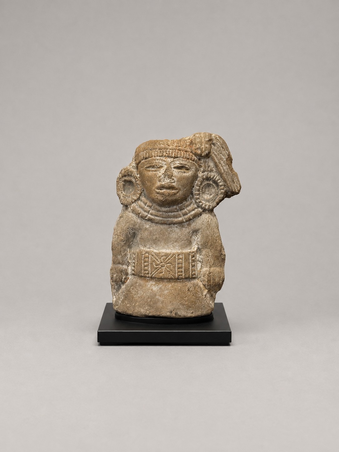 Pre-Columbian stone sculpture displayed upright on a custom black powder-coated steel mount, viewed from the front